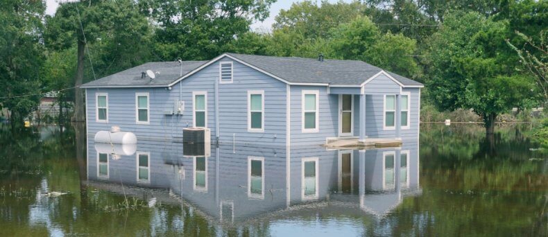 flooded home half submerged in water with trees in the background