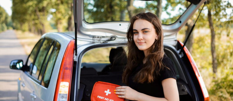 young woman standing behind car with first aid kit