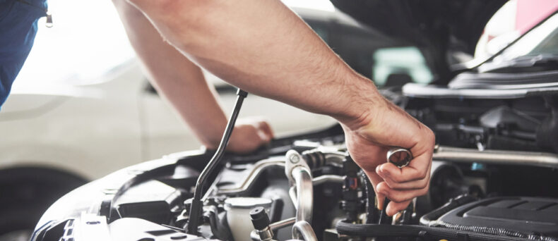 close up of hands doing maintenance under hood of car