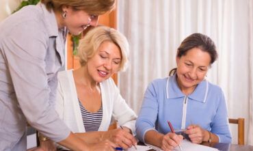 Two happy mature ladies sign life insurance documents