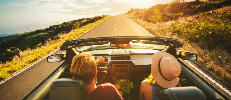 couple driving down road in convertible with the top down