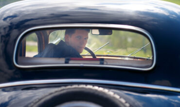 man looks back through the rear window of a classic car