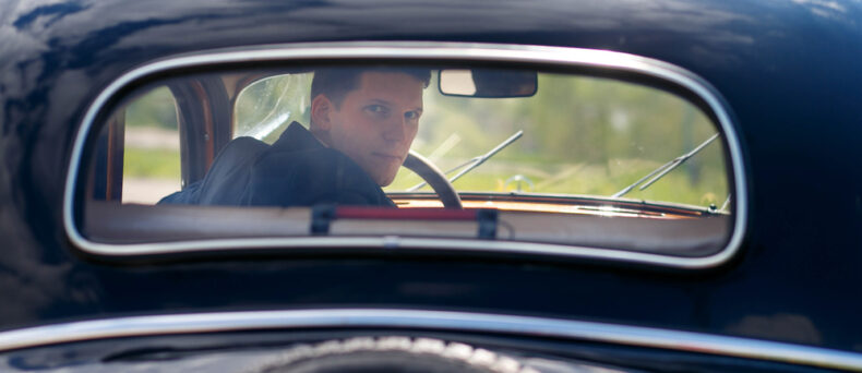 man looks back through the rear window of a classic car