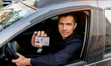 Man behind the wheel looking out window and holding up his driver's license - car insurance in Georgia