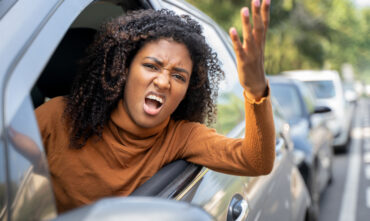 Angry young woman leans out driver's side window yelling - cheap car insurance in Georgia
