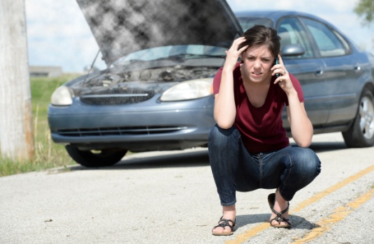 Woman worried in front of her car because it is overheated