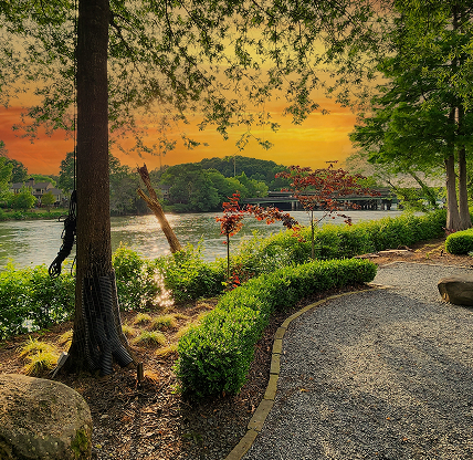 A gorgeous spring landscape along the Chattahoochee River with lush green trees, grass and plants and colorful flowers with powerful clouds at sunset at Ray’s on the River in Sandy Springs – cheap car insurance in Georgia.