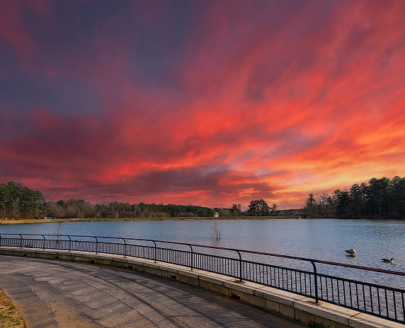 a gorgeous winter landscape at Rhodes Jordan park with a blue lake, yellow winter grass lush green trees, people walking and powerful clouds at sunset in Lawrenceville - cheap car insurance in Georgia.