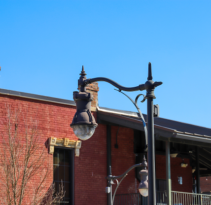 A tall curved black light post in front of a red brick building with a black metal balcony with bare winter trees and blue sky and powerful clouds at sunset in Douglasville - cheap car insurance in Georgia.