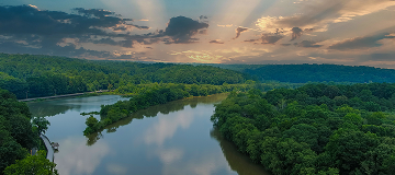 A stunning aerial shot of the still brown waters of the Chattahoochee river surrounded by vast miles of lush green trees with powerful clouds at Roswell Riverwalk Boardwalk in Roswell - cheap car insurance in Georgia.