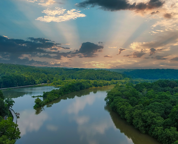 A stunning aerial shot of the still brown waters of the Chattahoochee river surrounded by vast miles of lush green trees with powerful clouds at Roswell Riverwalk Boardwalk in Roswell - cheap car insurance in Georgia.