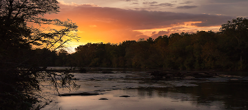 sunrise over the Chattahoochee River in Newnan Georgia surrounded by silhouette of fall foliage, sunlight glistening off river water - cheap car insurance in Georgia.
