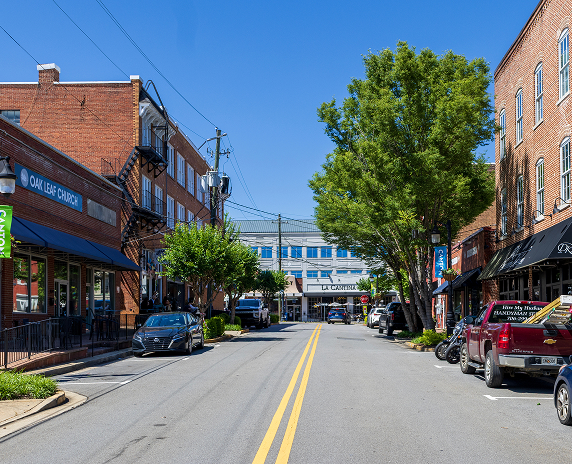 Street view of historic downtown Canton, Georgia with brick storefronts, local shops, and parked cars along a walkable main road.