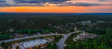 An aerial sunset view of downtown Evans, Georgia, showing roads, neighborhoods, and surrounding trees as the city transitions from day to evening.