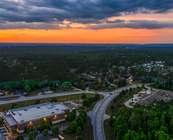 An aerial sunset view of downtown Evans, Georgia, showing roads, neighborhoods, and surrounding trees as the city transitions from day to evening.