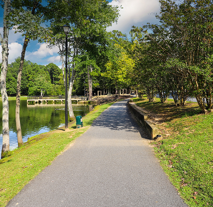 Paved walking path along a calm pond surrounded by trees at Huddleston Pond Park in Peachtree, Georgia