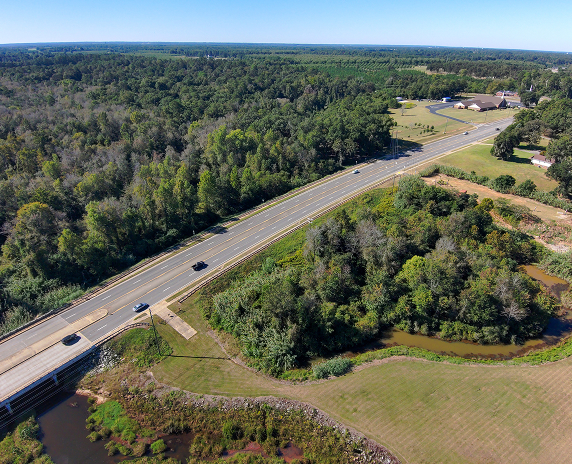 An aerial view of a highway cutting through wooded and rural landscapes, illustrating transportation and surrounding countryside near Perry, Georgia.